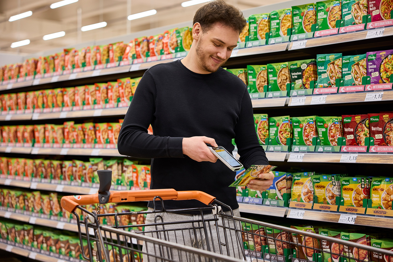 Junger Mann scannt Produkt mit einem mobilen Scan-Gerät vor einem Supermarktregal