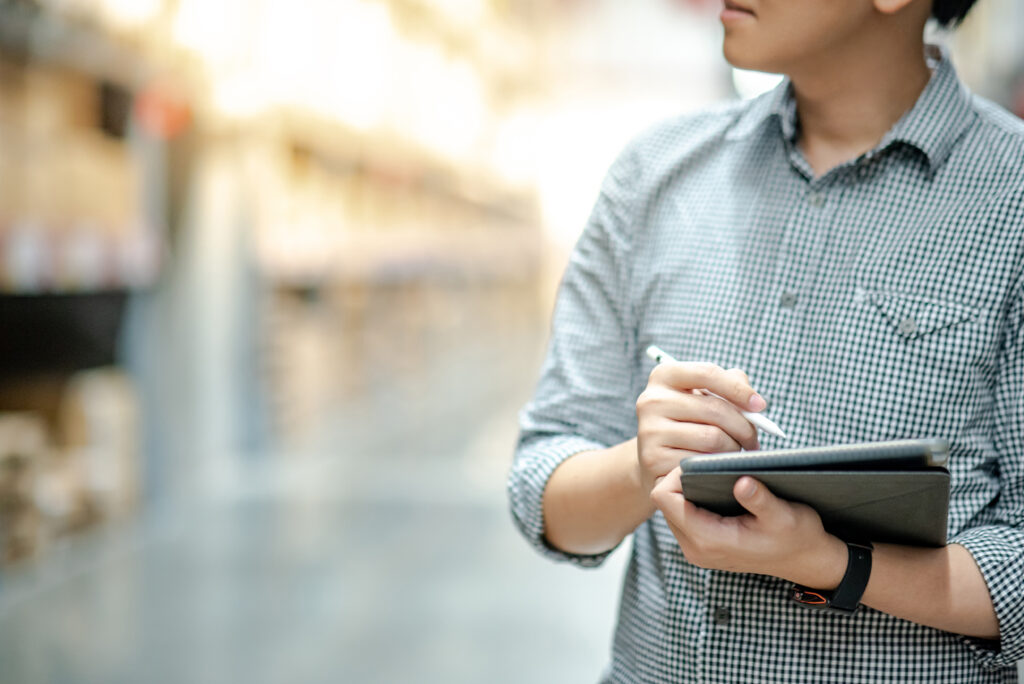Junger Mann in der Filiale mit Tablet, auf dem die Warenwirtschaft läuft